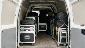Matériel audiovisuel protégé dans des caisses et chariots de transport, rangés dans un utilitaire événementiel ouvert.